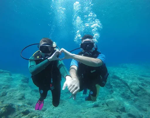 Why the Maldives is one of the most peaceful places on earth for night diving two people scuba diving underwater, making a heart shape with their hands.