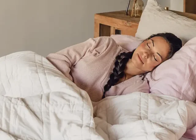 Woman peacefully sleeping under a white quilt on a cozy bed.