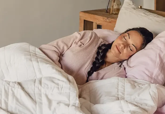 Woman peacefully sleeping under a white quilt on a cozy bed.