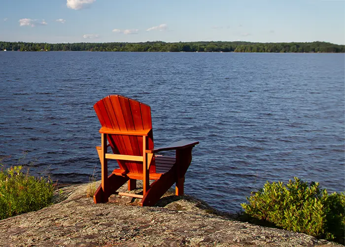 empty-red-muskoka-adirondack-chair-rocky-shoreline-along-lake-muskoka-ontario copy