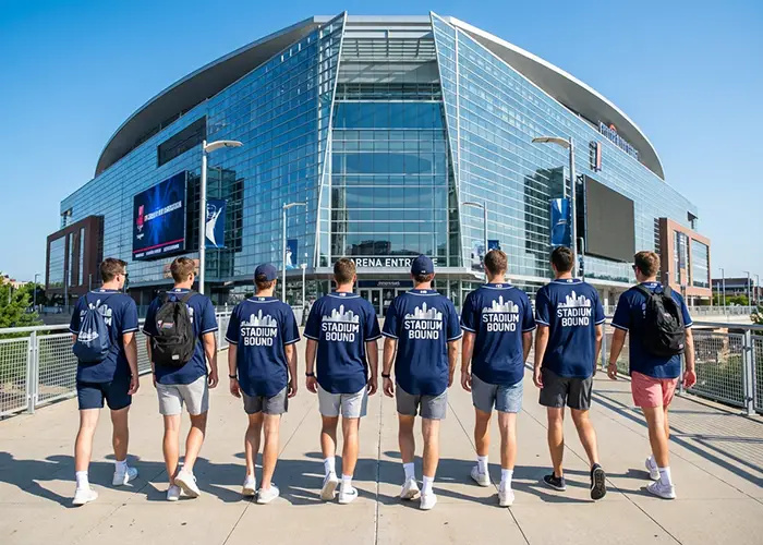 group of people walking toward stadium entrance in matching shirts.