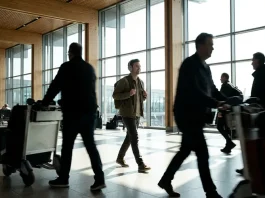People walking in an airport terminal with large windows.