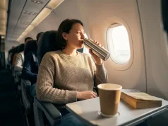 5 Comfort First Travel Tips for Better Sleep Person in airplane seat enjoying a drink from a thermos.