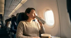 5 Comfort First Travel Tips for Better Sleep Person in airplane seat enjoying a drink from a thermos.