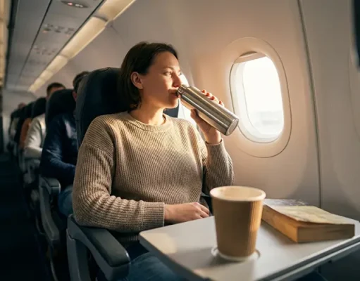 5 Comfort First Travel Tips for Better Sleep Person in airplane seat enjoying a drink from a thermos.