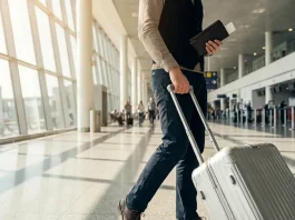 A person walking in an airport with a suitcase and a passport.