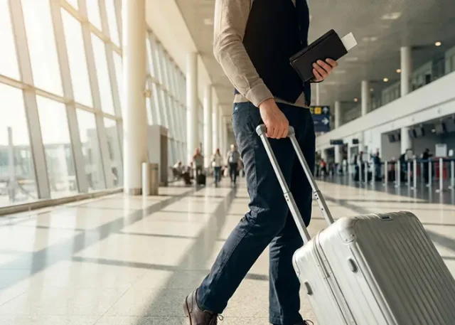 A person walking in an airport with a suitcase and a passport.