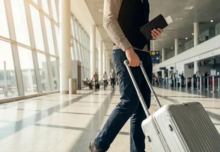 A person walking in an airport with a suitcase and a passport.