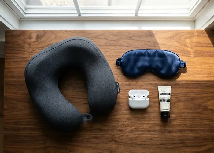 travel essentials neck pillow, eye mask, earbuds, and hand cream.