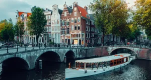 How to elevate your Amsterdam experience with the ultimate luxury event on the water Amsterdam canals with white cruise boat bridge and typical dutch houses