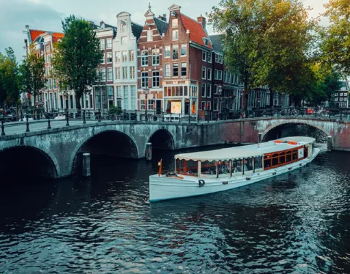 How to elevate your Amsterdam experience with the ultimate luxury event on the water Amsterdam canals with white cruise boat bridge and typical dutch houses