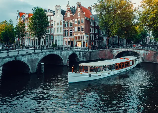 Amsterdam canals with white cruise boat bridge and typical dutch houses