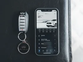 A car key fob lying on gravel beside the wheel of a parked car