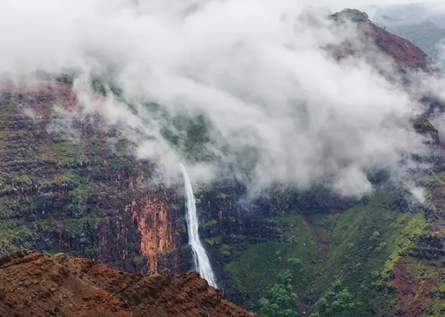 A scenic view of a tall waterfall cascading down a steep mountain landscape covered in green foliage.