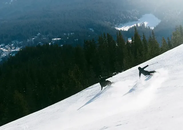 Skier and snowboarder descending a snowy slope at LAAX ski resort in the Swiss Alps