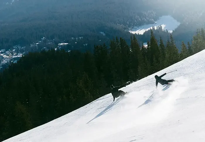 Skier and snowboarder descending a snowy slope at LAAX ski resort in the Swiss Alps