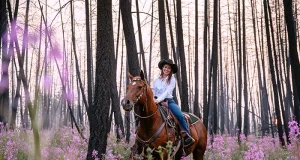 Five Learning Vacations That Turn Family Travel Into an Adventure Horseback rider traveling through pink wildflowers in a recovering forest landscape after a wildfire
