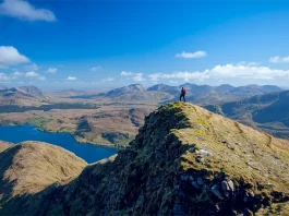 Walker on the South Ridge of Mweelrea Mountain overlooking Killary Fjord in County Mayo, Ireland, with panoramic views of mountains, lakes, and dramatic coastal landscapes.
