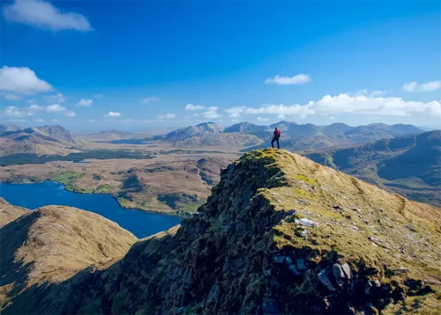 overlooking Killary Fjord copy Walker on the South Ridge of Mweelrea Mountain overlooking Killary Fjord in County Mayo, Ireland, with panoramic views of mountains, lakes, and dramatic coastal landscapes.