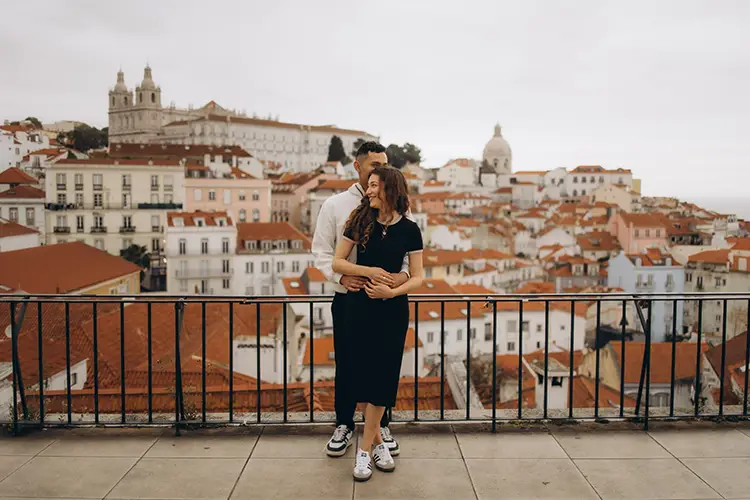 Couple at an Alfama viewpoint with the rooftops of Lisbon and the São Vicente de Fora monastery behind them