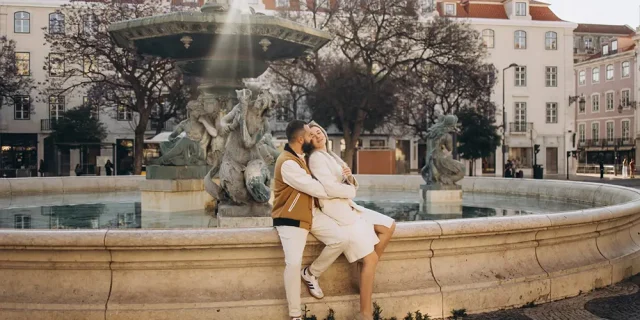 Couple sitting on the rim of the baroque fountain in Rossio square, Lisbon