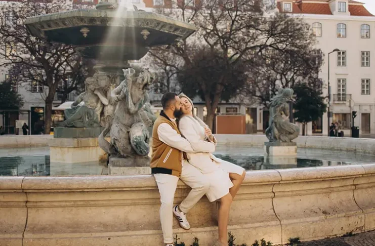 Couple sitting on the rim of the baroque fountain in Rossio square, Lisbon