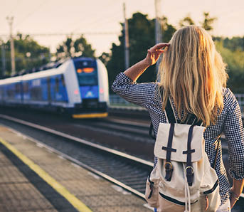 Woman is looking at arriving train at a railway station. Backpacker travelling through Europe by train. 