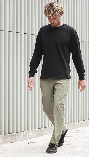 A man wearing a black shirt and green pants is walking down a sidewalk. Description generated by AI