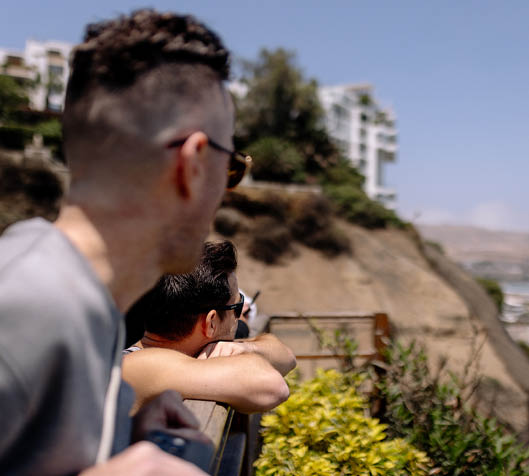 Three men are sitting on a bench overlooking the ocean. Description generated by AI