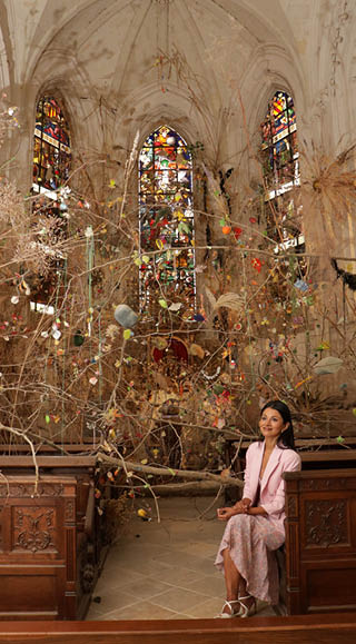 A woman is standing in front of a church with a large stained glass window. Description generated by AI