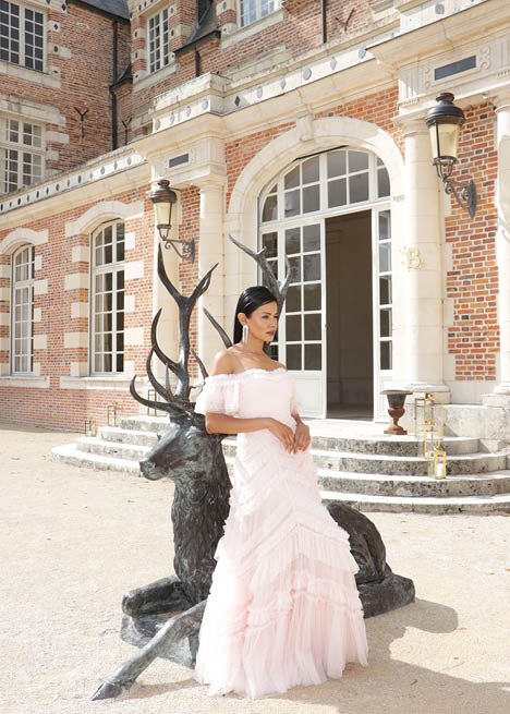 A woman in a pink dress standing in front of a building. Description generated by AI