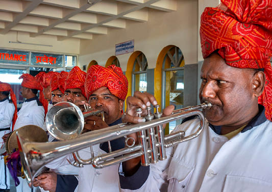 A group of men wearing red turbans and white shirts are playing musical instruments. Description generated by AI