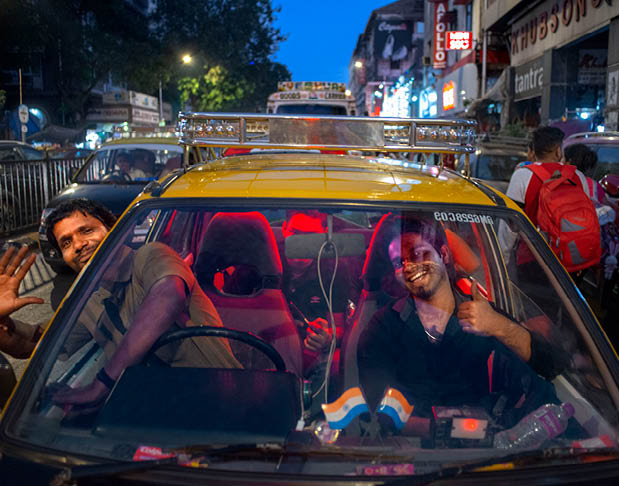 A yellow taxi cab with two men in it. Description generated by AI
