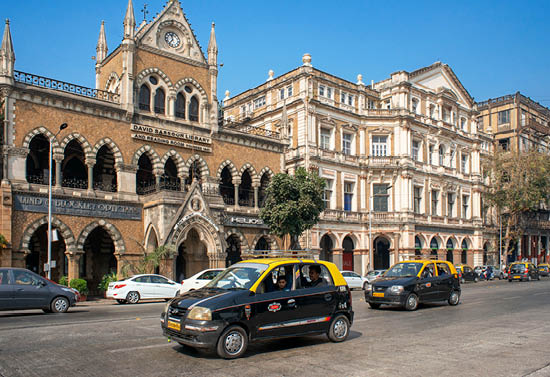 A black car is driving down a street in front of a building. Description generated by AI