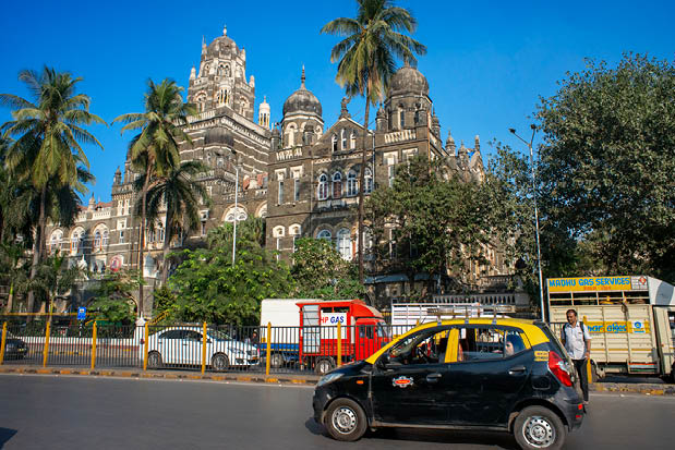 A black car is driving on a street in front of a large building. Description generated by AI