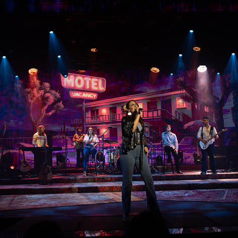 A stage with a hotel sign and a man singing. Description generated by AI