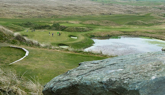A large rock in a field with a pond in the background. Description generated by AI