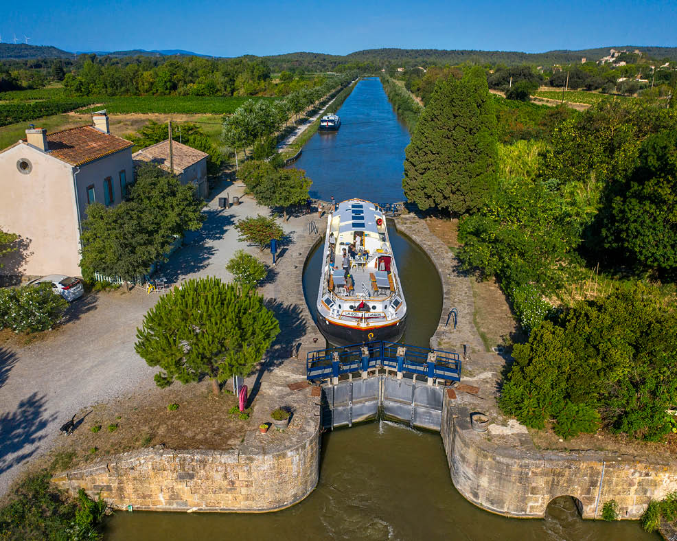 Aerial view of a big boat crossing cluse d´Argens argens look. Canal du Midi at village of Argens-Minervois Aude South of France southern waterway waterways holidaymakers queue for a boat trip on the river, France, Europe  Tour with a rental boat from the Le Boat company from Homps to the nine Fonseranes locks in B ziers and back to Carcassonne.  