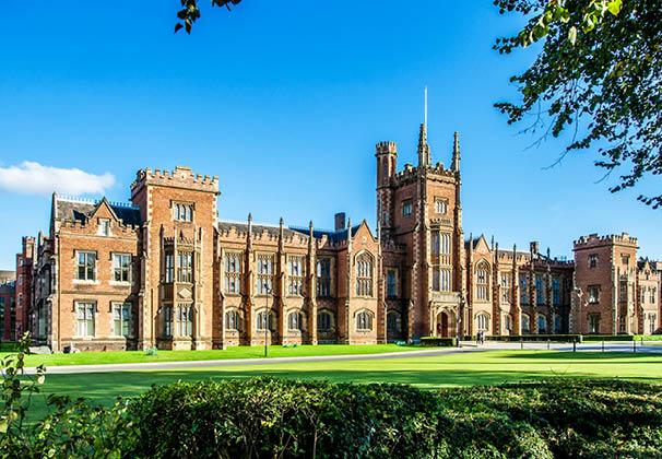 The Queen's University of Belfast with a grass lawn, tree branches and a hedge in sunset light