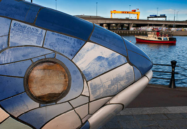 The Big Fish sculpture by John Kindness, Donegall Quay, River Lagan, Belfast, Northern Ireland, UK. Back, The Red Hulled Tourist Boat Mona Moored in The River Lagan. The Big Fish also called the Bigfish is a printed ceramic mosaic sculpture by John Kindness 10 metres long constructed in 1999 in Donegall Quay in Belfast, near the Lagan Lookout and Custom House. 