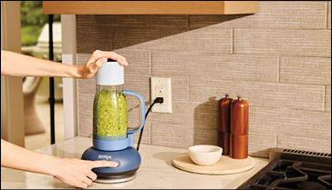 A person is holding a green blender on a counter. AI generated content