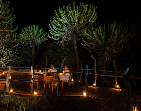 A group of people are sitting around a table in a dark room, with lit candles providing the light. AI generated content
