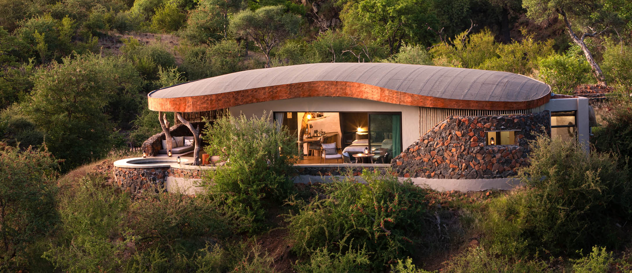 A house with a unique design, made of stone and wood, is situated in a forest. The house has a large roof and is surrounded by trees. AI generated content