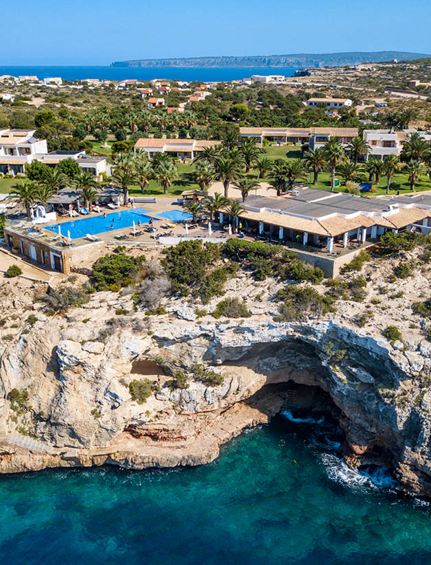 A large rock formation with a blue pool in the middle, surrounded by a resort with multiple buildings and palm trees. AI generated content