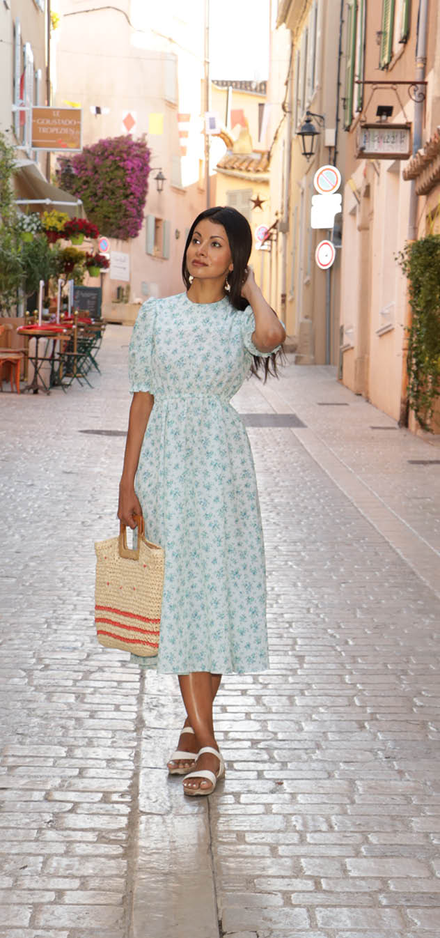 A woman in a flowered dress is standing on a cobblestone street, holding a brown bag. AI generated content