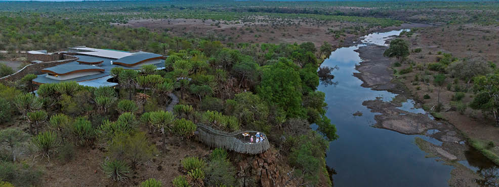 A man and woman are standing on a wooden deck overlooking a river. AI generated content
