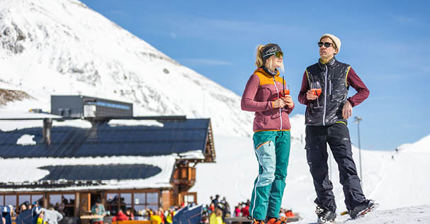 Two people standing on a snowy hill with a building in the background. AI generated content