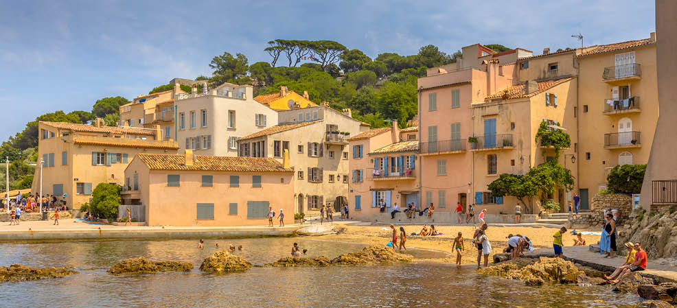 A group of people are enjoying a day at the beach, with some swimming in the water and others sitting on the shore. The beach is located near a city, as evidenced by the presence of buildings in the background. AI generated content