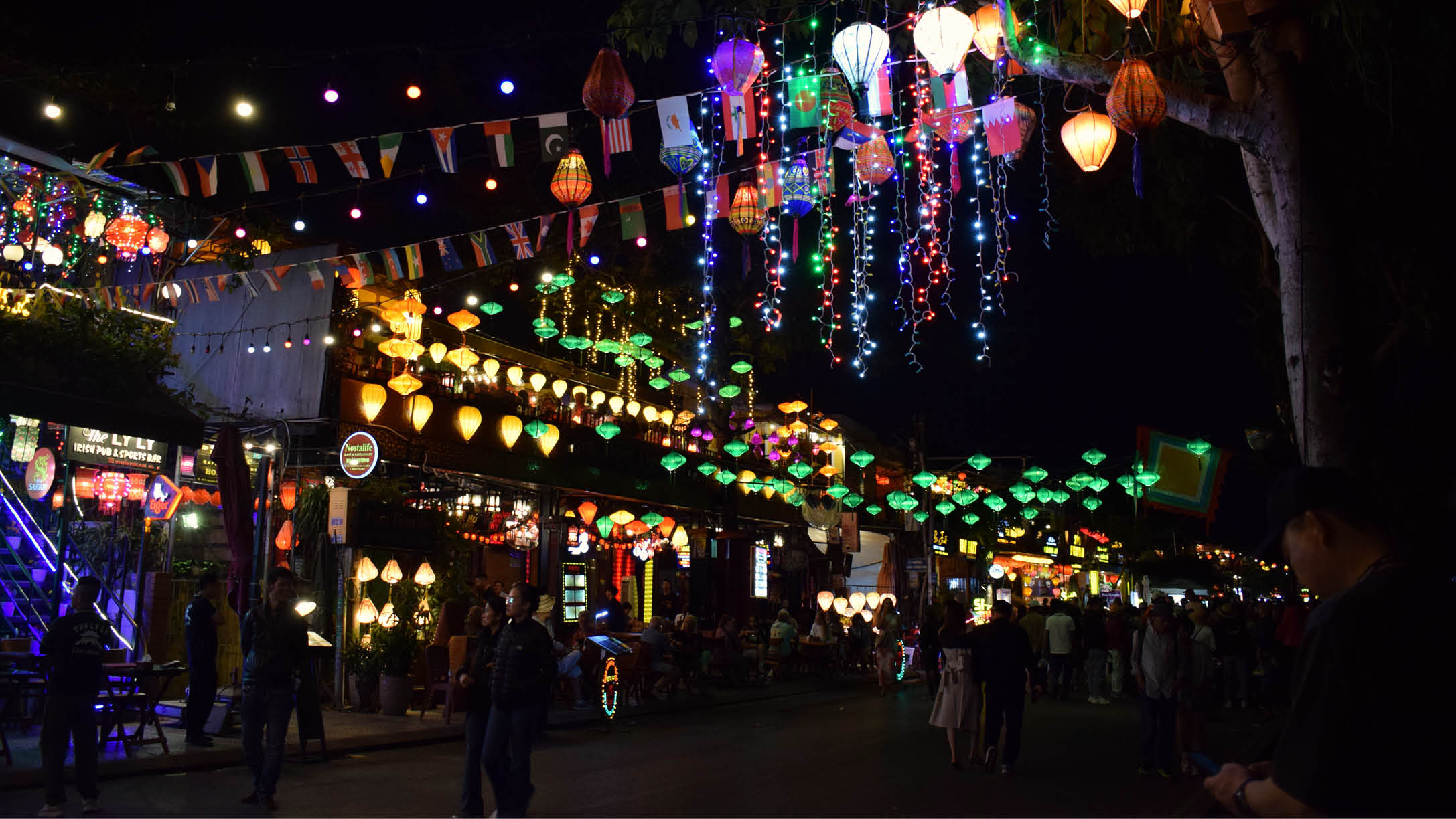 A street is illuminated with colorful lights and lanterns, creating a festive atmosphere. People are walking around, enjoying the display. AI generated content