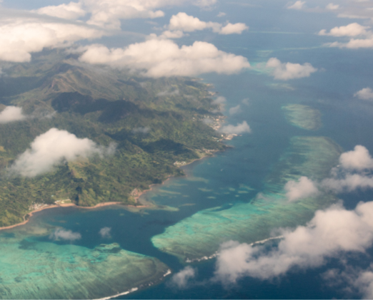 The view of a Fiji island landscape and the coral reef surrounding it from above the clouds.
